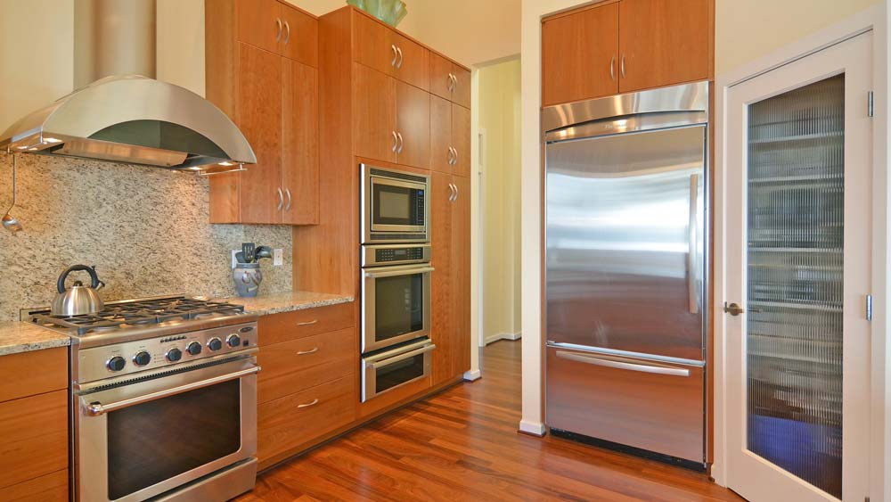 A kitchen with stainless steel appliances including an oven, vent hood, and refrigerator.